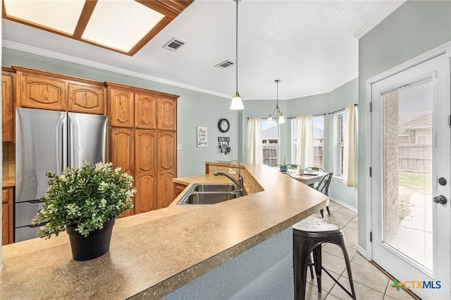 kitchen with visible vents, crown molding, freestanding refrigerator, light tile patterned flooring, and a sink