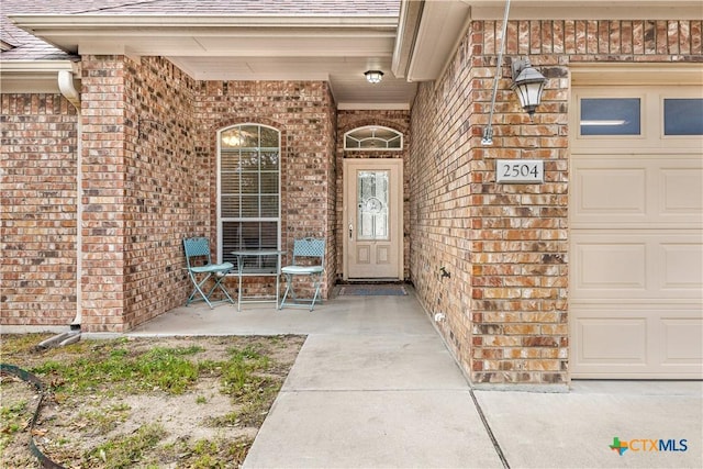 doorway to property featuring a garage, brick siding, and a shingled roof