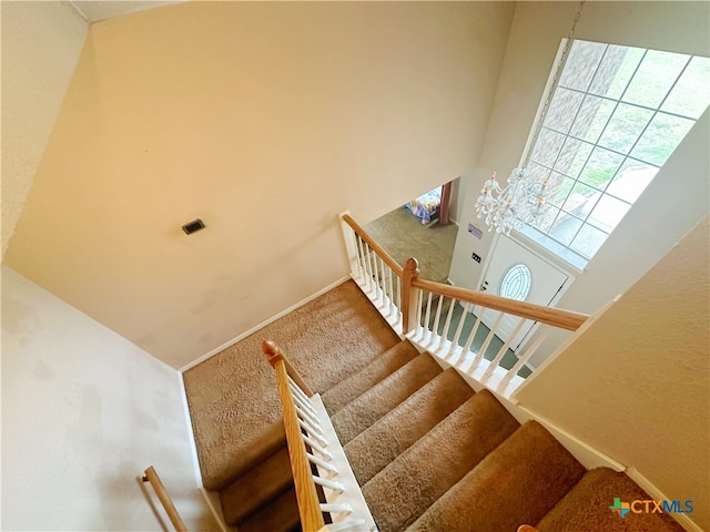 staircase with a towering ceiling, a notable chandelier, and carpet floors