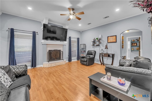 living room with a brick fireplace, wood-type flooring, ceiling fan, and ornamental molding