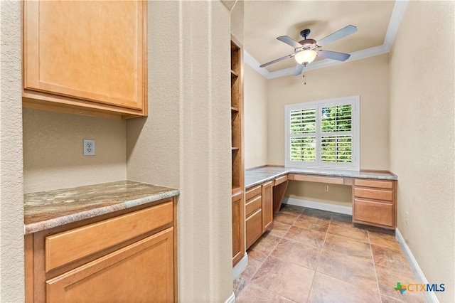 interior space featuring baseboards, built in desk, ceiling fan, crown molding, and light stone countertops