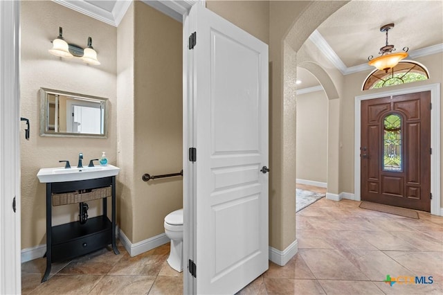 foyer featuring arched walkways, light tile patterned floors, baseboards, and crown molding