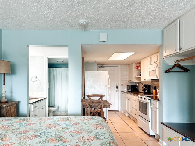 bedroom featuring white refrigerator, a textured ceiling, light tile patterned floors, and ensuite bathroom