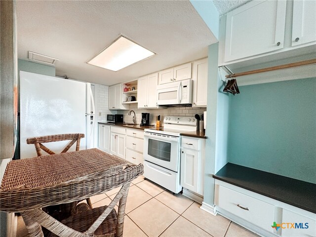 kitchen with white cabinets, white appliances, light tile patterned floors, and backsplash