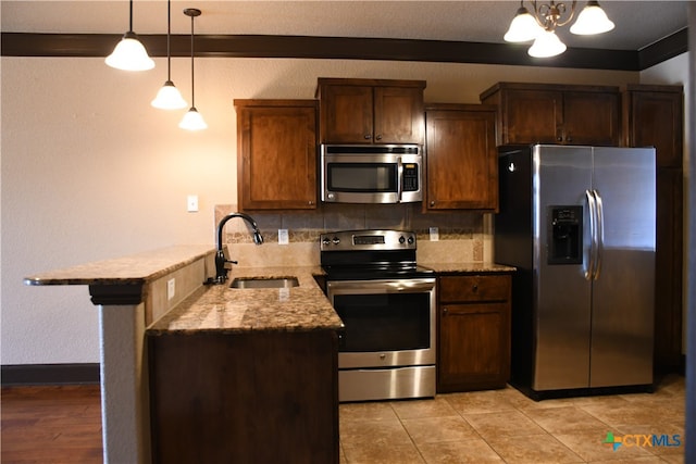 kitchen with kitchen peninsula, appliances with stainless steel finishes, backsplash, sink, and pendant lighting