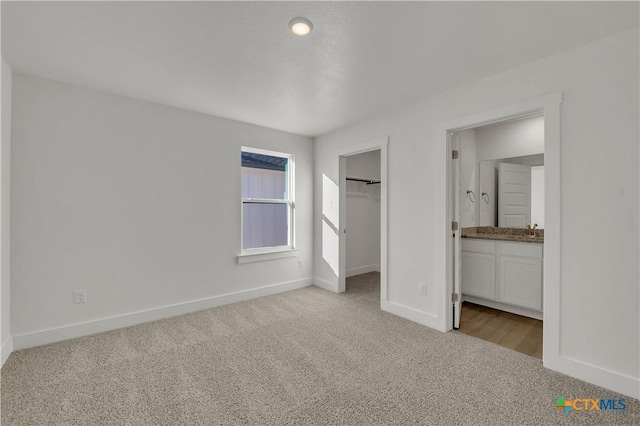 unfurnished bedroom featuring light carpet, sink, a walk in closet, and ensuite bathroom