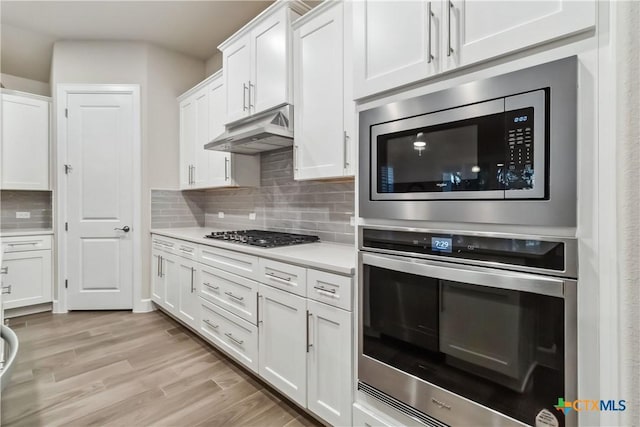 kitchen featuring tasteful backsplash, light wood-type flooring, white cabinets, and appliances with stainless steel finishes