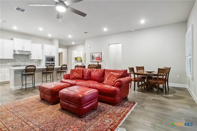 living room with ceiling fan, sink, and light wood-type flooring