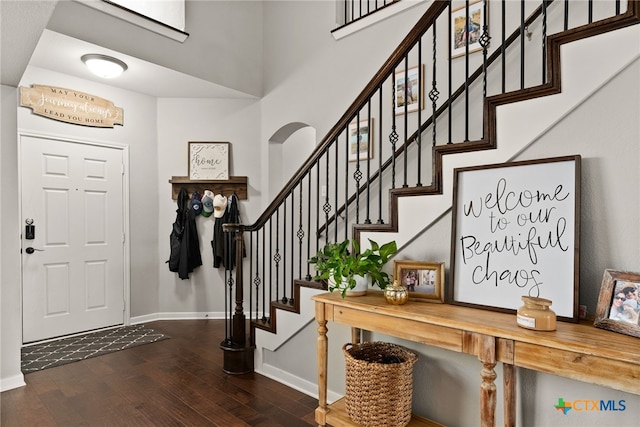 entrance foyer with arched walkways, stairway, wood finished floors, and baseboards