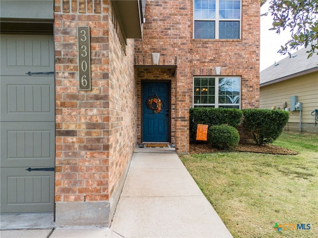 doorway to property with a yard and brick siding