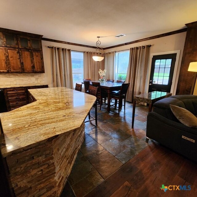 11710 Uplands Ridge Dr, Austin, TX 78738 - kitchen featuring ornamental molding, stone tile floors, decorative light fixtures, dark brown cabinetry, and a center island