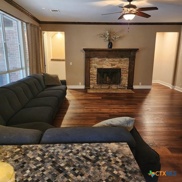 living room with ornamental molding, a stone fireplace, dark hardwood / wood-style floors, and ceiling fan