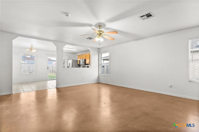 unfurnished living room with visible vents, plenty of natural light, baseboards, and ceiling fan with notable chandelier