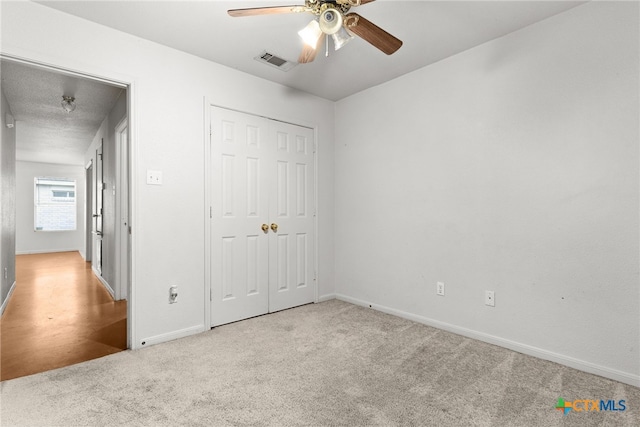 unfurnished bedroom featuring a closet, light colored carpet, and ceiling fan