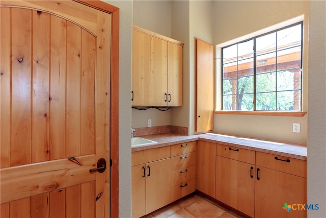 kitchen with light tile patterned flooring, light brown cabinetry, and sink