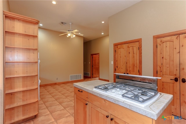 kitchen with light tile patterned flooring, a kitchen island, light brown cabinets, tile counters, and ceiling fan