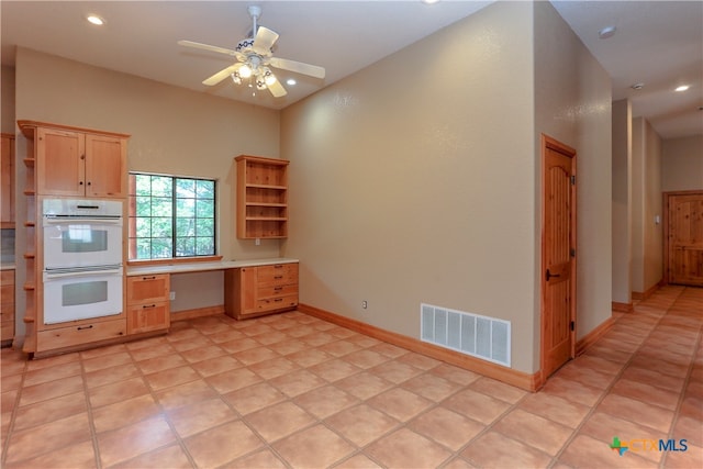 kitchen featuring light brown cabinetry, light tile patterned flooring, ceiling fan, double oven, and built in desk