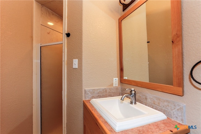 bathroom with a shower with door, vanity, and decorative backsplash