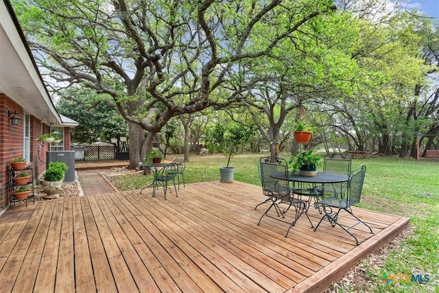 deck with outdoor dining area, cooling unit, and a yard