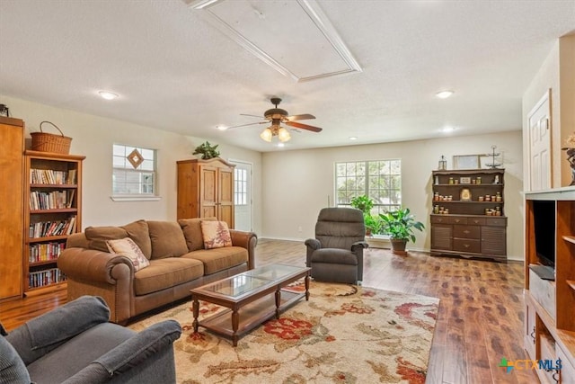 living area featuring attic access, baseboards, a textured ceiling, a ceiling fan, and wood finished floors
