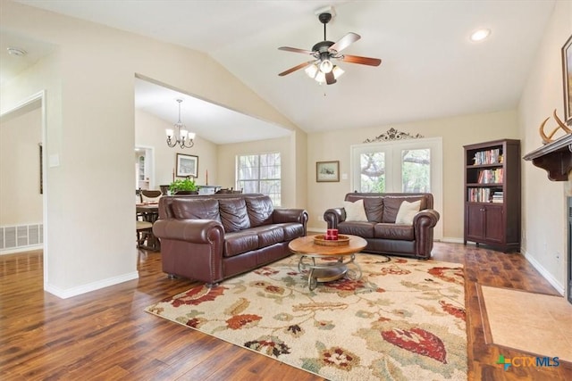 living room featuring lofted ceiling, ceiling fan with notable chandelier, baseboards, visible vents, and wood finished floors