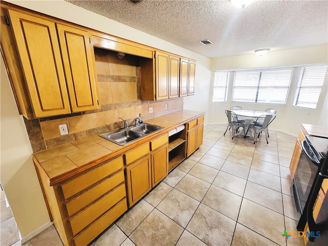 kitchen featuring backsplash, range with electric cooktop, sink, tile counters, and light tile patterned flooring