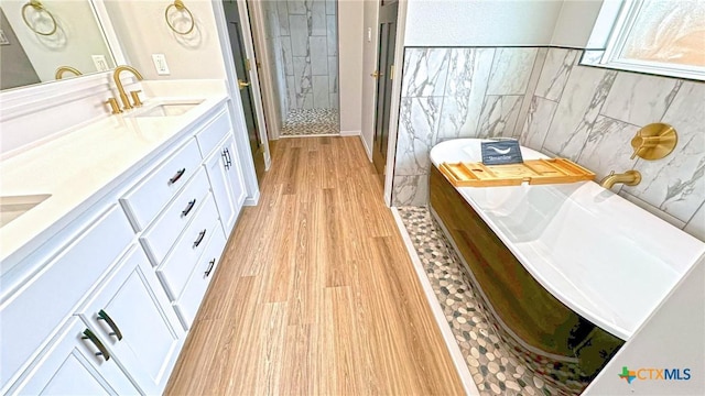 bathroom featuring tile walls, double vanity, a stall shower, a sink, and wood finished floors