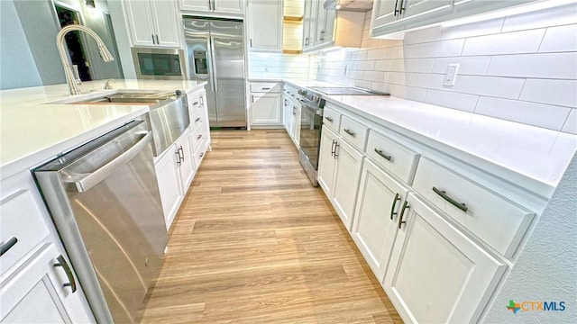 kitchen featuring stainless steel appliances, light wood finished floors, backsplash, and light countertops