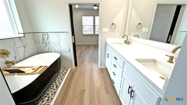 full bathroom with double vanity, a soaking tub, wood finished floors, a sink, and tile walls