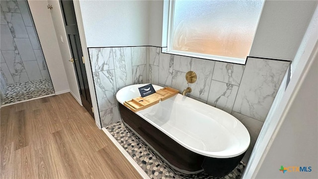 full bath featuring a freestanding tub, wood finished floors, tile walls, tiled shower, and washer / dryer