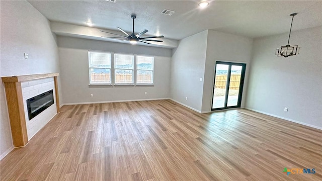 unfurnished living room featuring light wood-type flooring, a glass covered fireplace, visible vents, and ceiling fan with notable chandelier