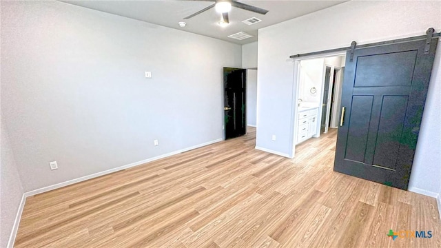 unfurnished bedroom featuring visible vents, a barn door, a ceiling fan, light wood-type flooring, and baseboards