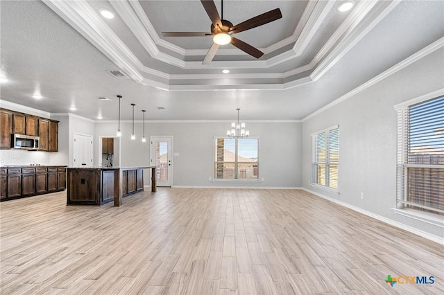 kitchen featuring a center island with sink, decorative light fixtures, a raised ceiling, and crown molding