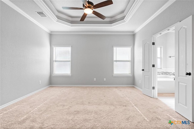 carpeted spare room with a tray ceiling, crown molding, ceiling fan, and a healthy amount of sunlight