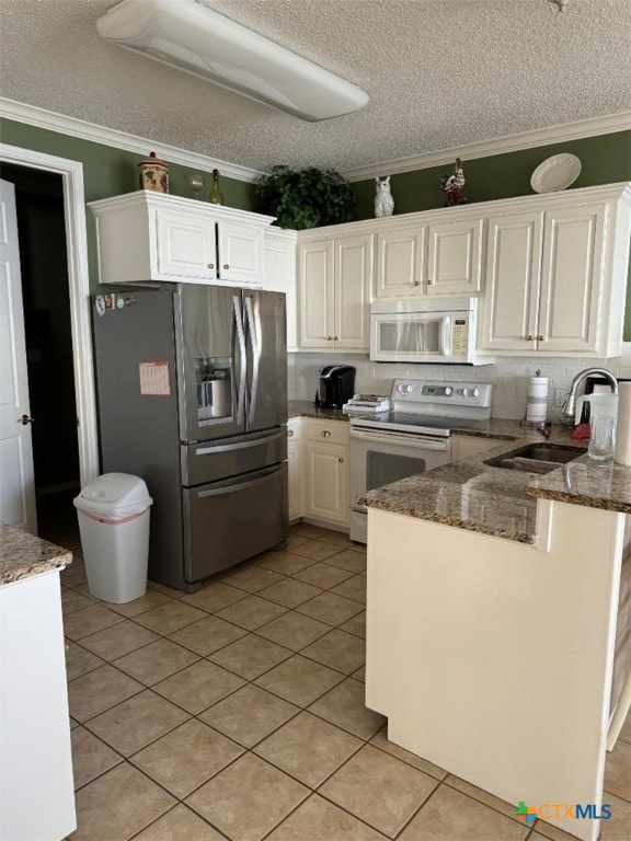 kitchen with sink, kitchen peninsula, dark stone counters, white appliances, and white cabinets