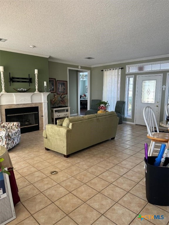 living room featuring light tile patterned floors, a textured ceiling, ornamental molding, and a tiled fireplace