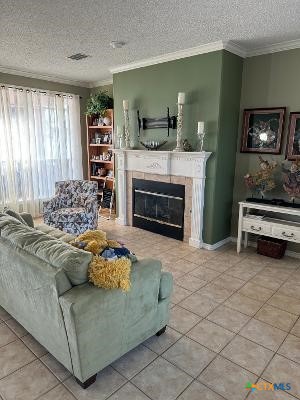 tiled living room featuring a textured ceiling, crown molding, and a fireplace