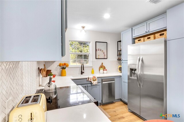 kitchen featuring tasteful backsplash, sink, stainless steel appliances, and light wood-type flooring