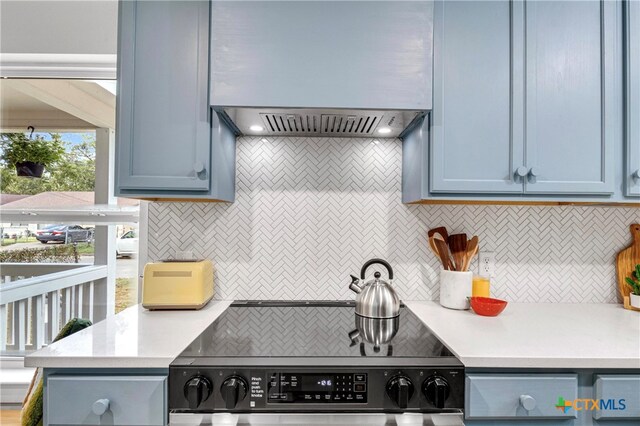 kitchen with blue cabinetry, range, tasteful backsplash, and wall chimney exhaust hood