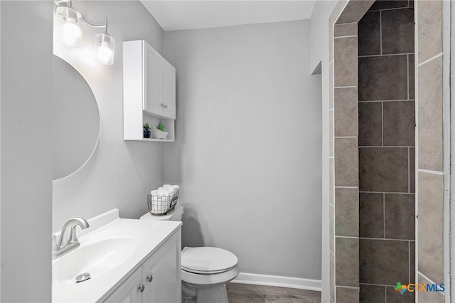 bathroom with wood-type flooring, vanity, toilet, and a tile shower