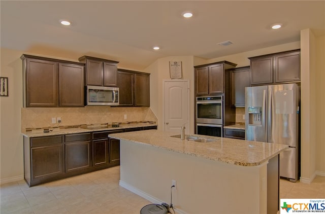 kitchen with stainless steel appliances, a center island with sink, decorative backsplash, dark brown cabinetry, and sink