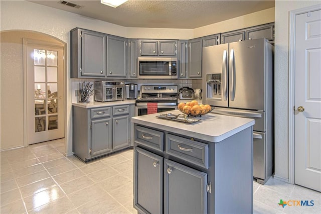 kitchen with light tile patterned flooring, a center island, a textured ceiling, appliances with stainless steel finishes, and gray cabinets