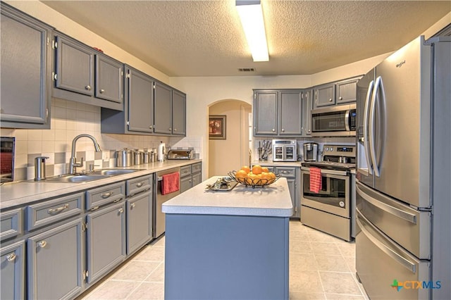 kitchen with a kitchen island, sink, gray cabinetry, light tile patterned floors, and stainless steel appliances