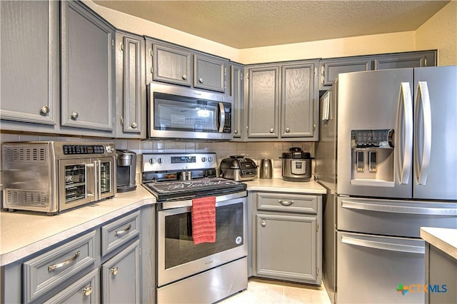 kitchen with gray cabinetry, light tile patterned floors, decorative backsplash, and stainless steel appliances