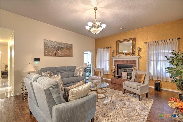 living room featuring dark wood-type flooring, a textured ceiling, a fireplace, and a chandelier