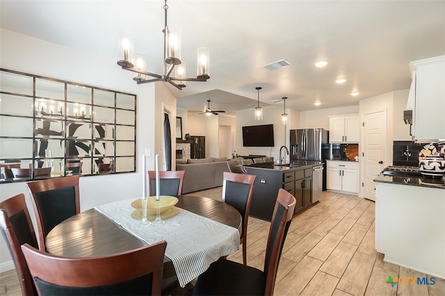 dining space featuring light wood-type flooring, sink, and ceiling fan with notable chandelier