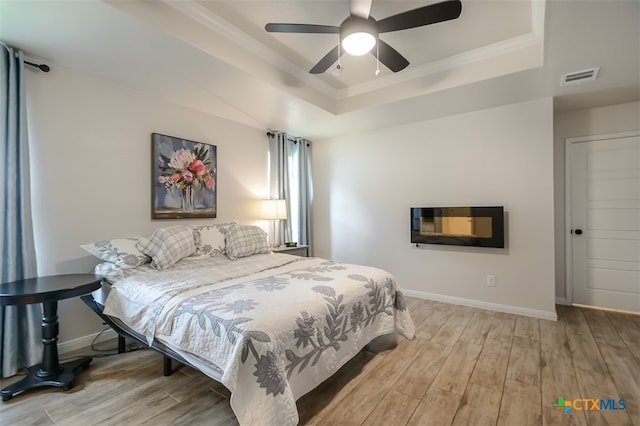 bedroom with light wood-type flooring, ceiling fan, and a tray ceiling