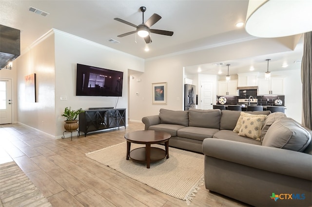 living room with light hardwood / wood-style floors, sink, ceiling fan, and crown molding