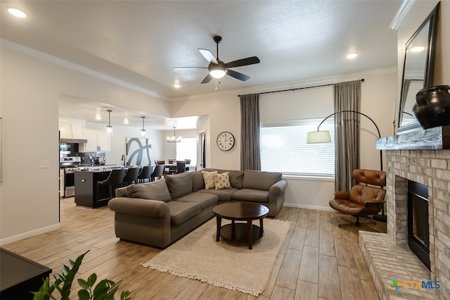 living room with a fireplace, ceiling fan with notable chandelier, crown molding, and light hardwood / wood-style flooring