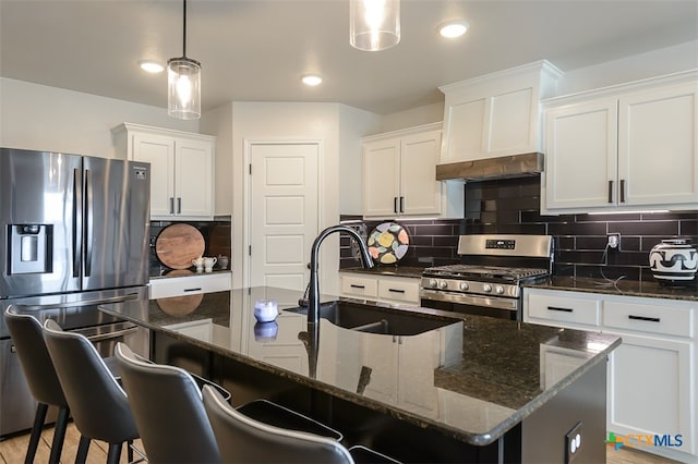 kitchen with stainless steel appliances, a center island with sink, decorative backsplash, pendant lighting, and dark stone countertops